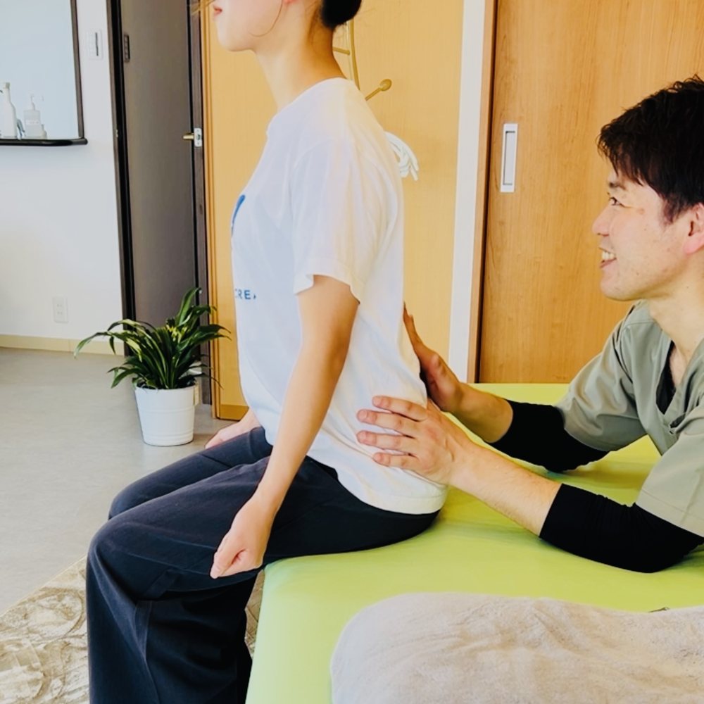 椅子に座った方の腰まわりに、院長が手を添えて、姿勢を一緒に確認している様子